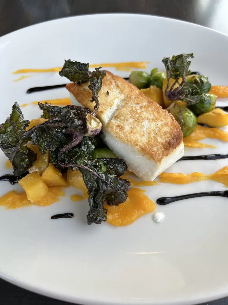 Cod (fish) on a plate with kale salad on the side.