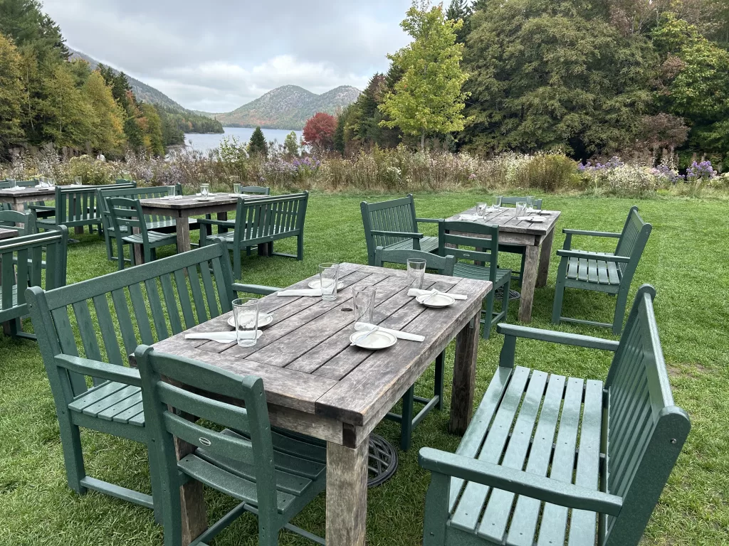 Tables and benches on the lawn with Jordan Pond and Bubbles mountains in the background