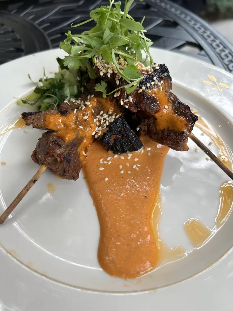 Beef skewers on a plate with green garnish.